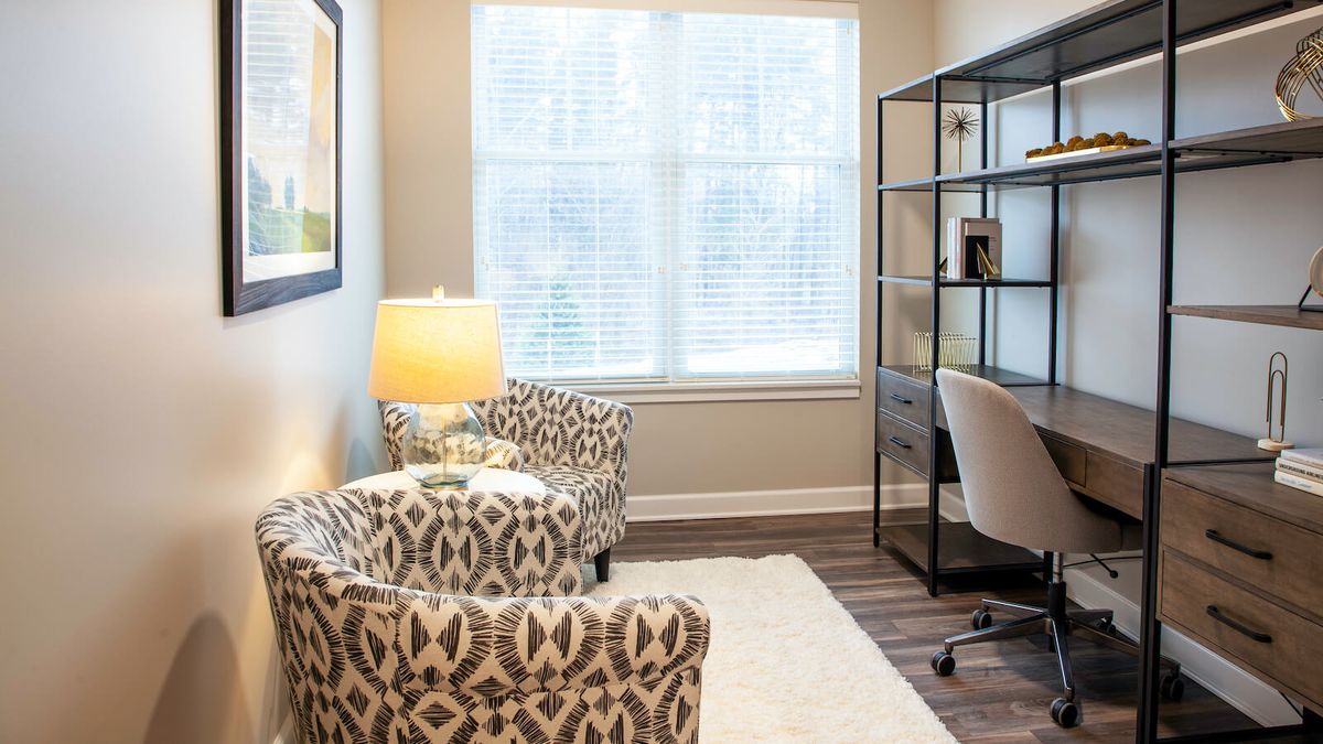 A modern office interior featuring patterned chairs, a desk with a chair, and a bookshelf.