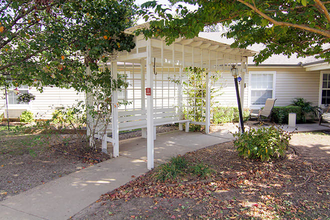 A cozy outdoor pergola with a bench offers a peaceful garden retreat along a paved pathway.