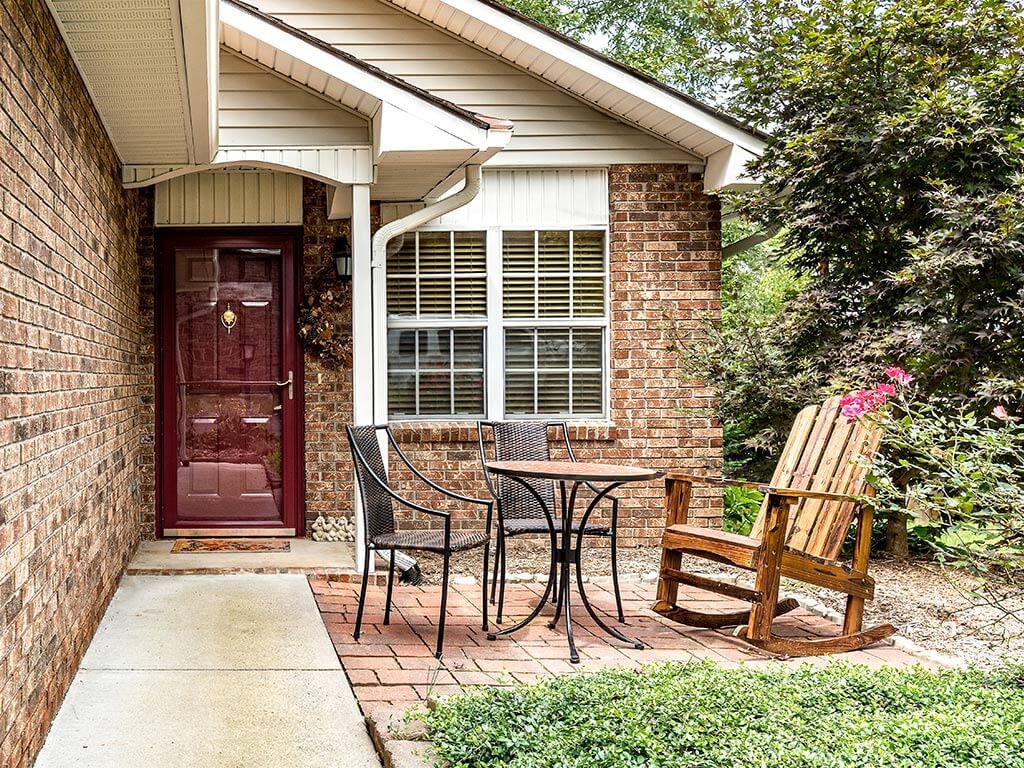 A cozy front patio with a small table, chairs, and a wooden rocker in front of a brick house.