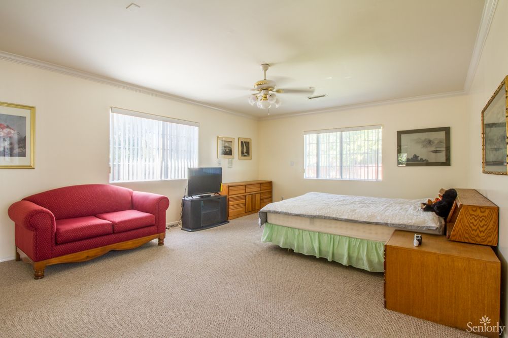 Spacious bedroom with a bed, red sofa, TV, and two large windows.