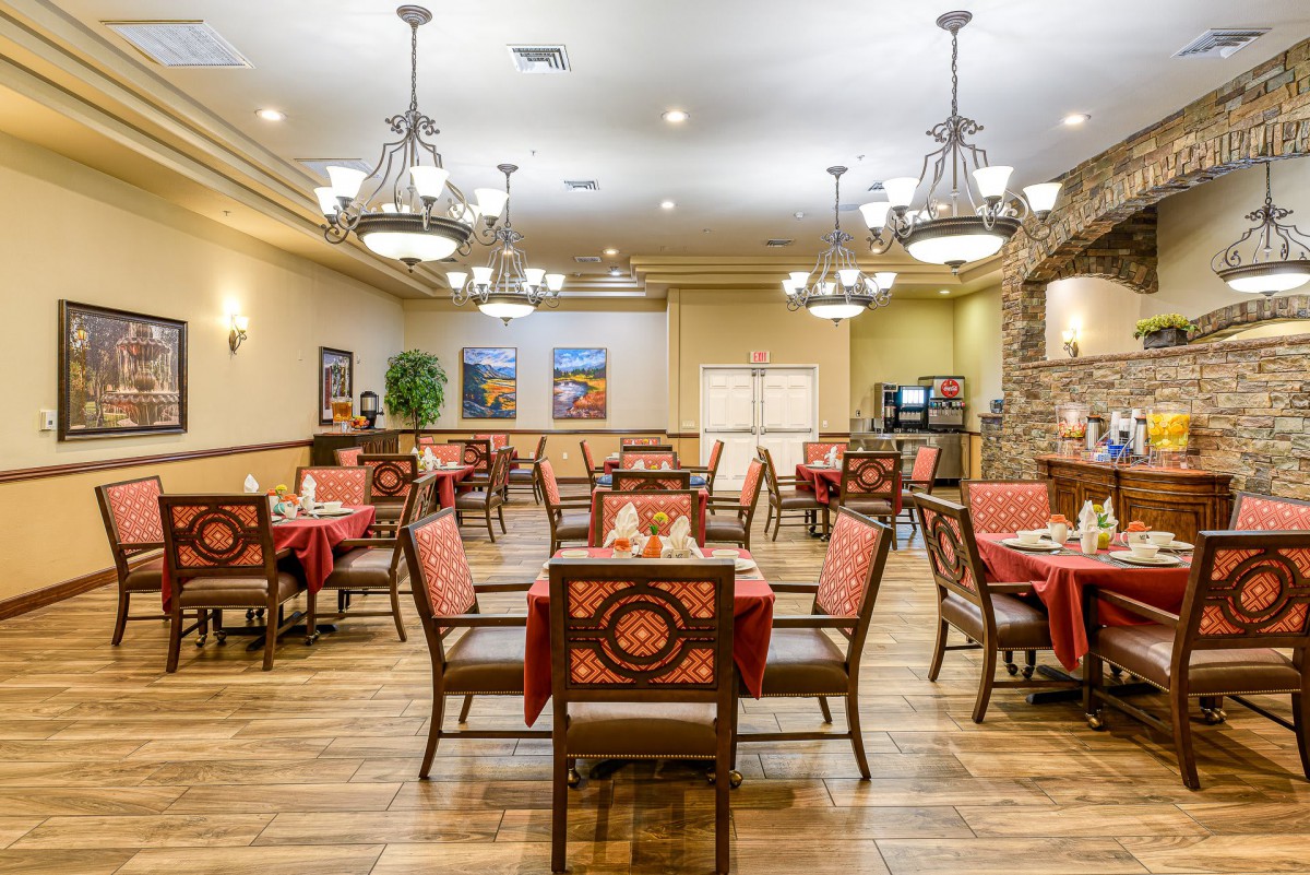 A spacious dining room with neatly arranged tables and chairs, featuring elegant chandeliers and warm lighting.