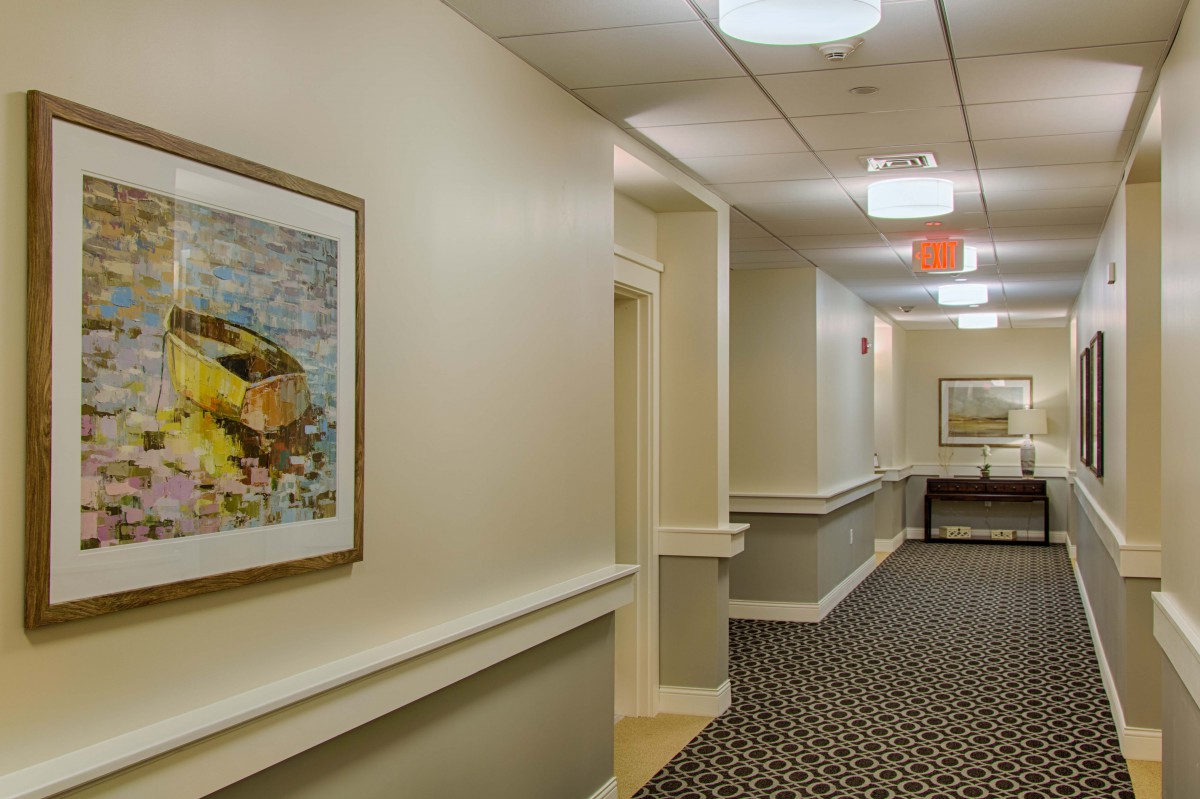 A well-lit hallway with framed artwork on the wall and patterned carpet flooring.