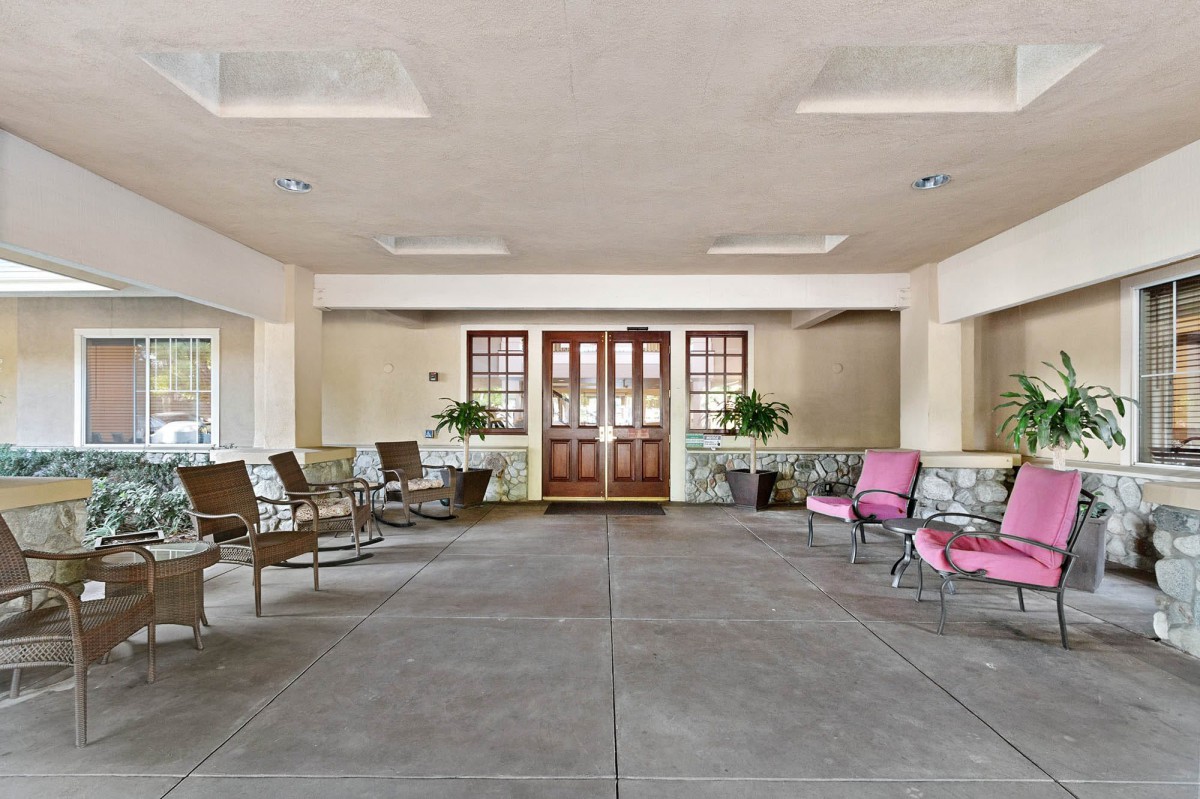 A spacious lobby area with chairs arranged along the walls, featuring large wooden doors and potted plants.