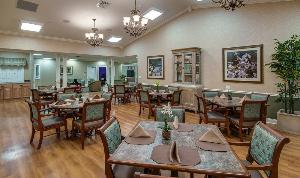 An elegantly set dining area with multiple tables and chairs, featuring chandeliers and tasteful decor.