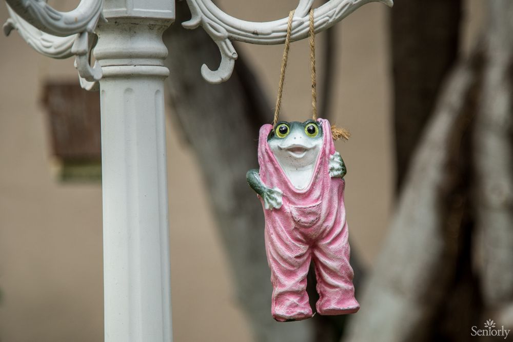 A whimsical frog sculpture in pink overalls hanging as a garden decoration.