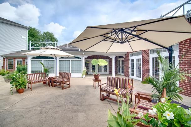 A spacious patio area with wooden seating and large umbrellas, surrounded by a brick building and decorated with potted plants.
