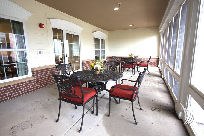 An outdoor patio with iron furniture and red cushions, featuring a table adorned with flowers.