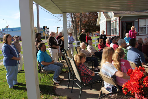 A community gathering taking place outdoors with people seated in chairs, enjoying a sunny day.