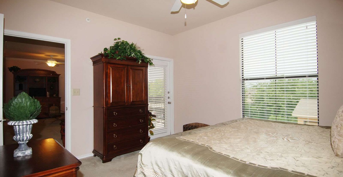 A tidy bedroom with a wooden wardrobe, large bed, and window with blinds.