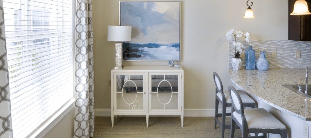 A modern interior setup featuring a white cabinet with a lamp and an abstract painting above it.