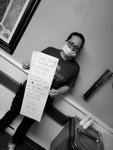 A person wearing a mask holds a sign in a hospital setting, conveying an important message.