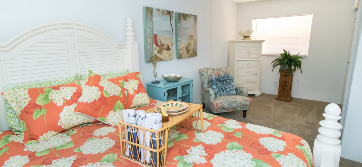 A cozy bedroom featuring floral bedding with a coastal theme, complemented by ocean-themed artwork and comfortable furniture.