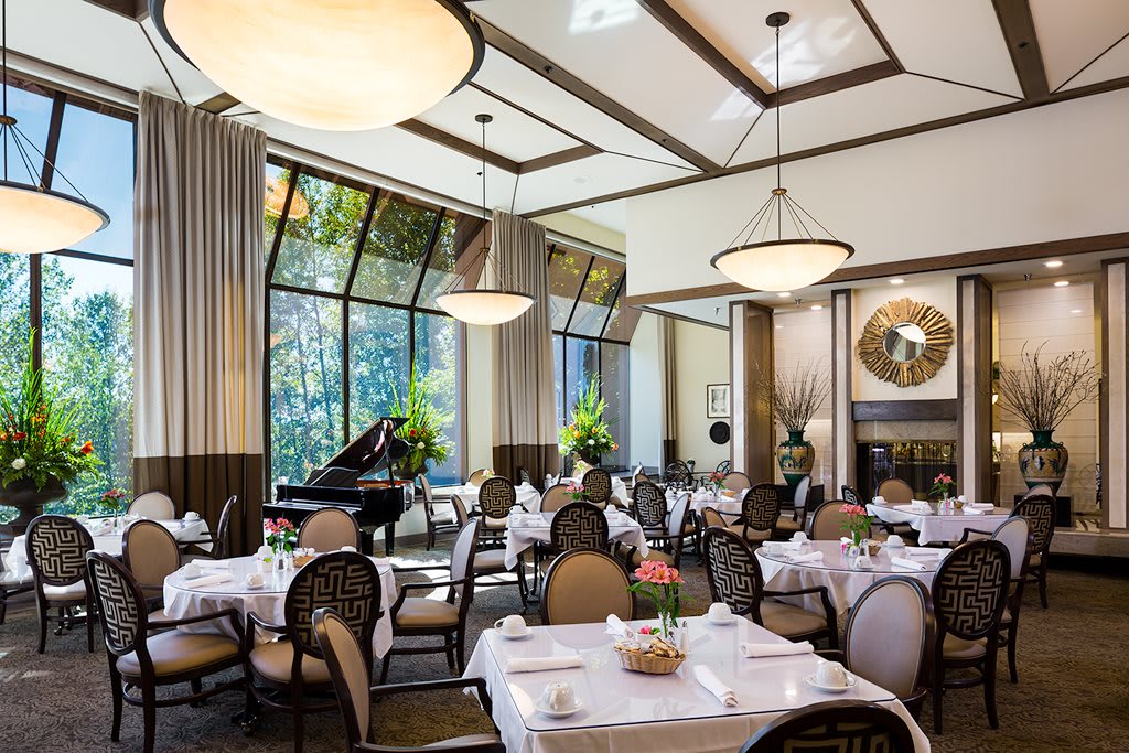 An elegant restaurant interior with neatly arranged tables, chandeliers, and a grand piano.