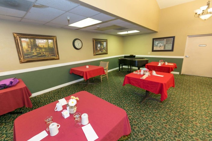 A dining room with tables covered in red tablecloths, decorated with paintings and set for a meal.