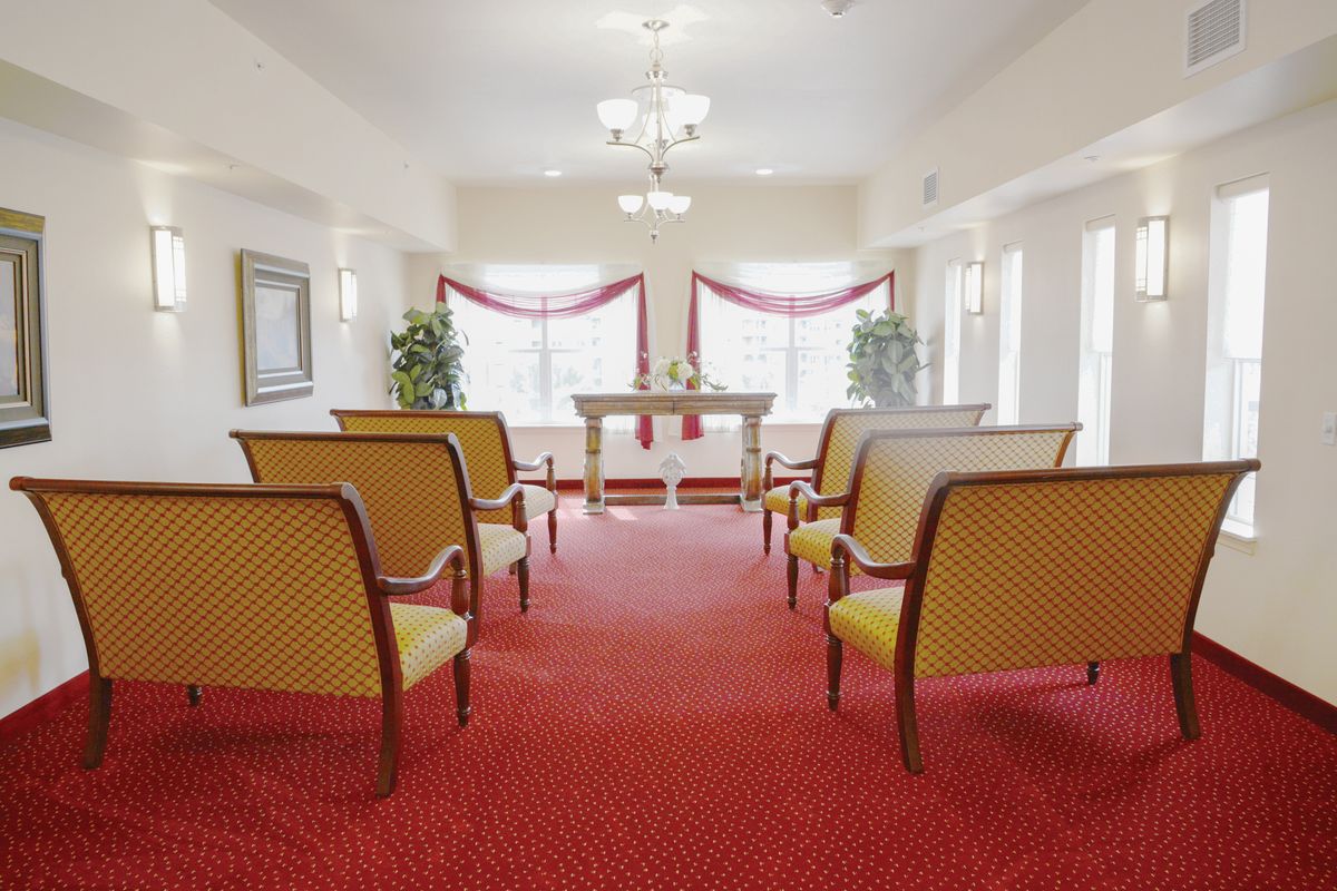 An elegant ceremony room with arranged chairs and a central altar, complemented by red carpeting and decorated windows.
