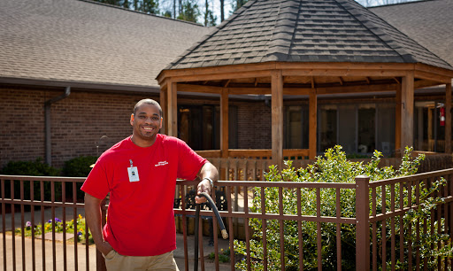 A person standing by a wooden fence, smiling in front of a gazebo.