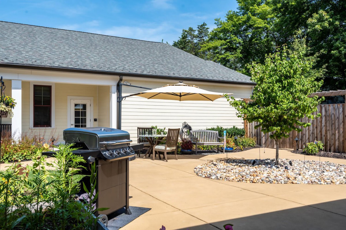 A well-maintained backyard patio featuring outdoor furniture, a grill, and a large umbrella on a sunny day.