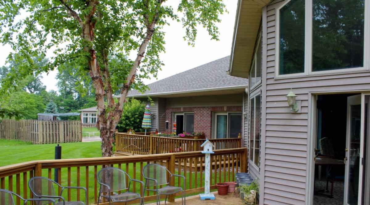 A peaceful backyard scene featuring a deck and garden area beside a house.