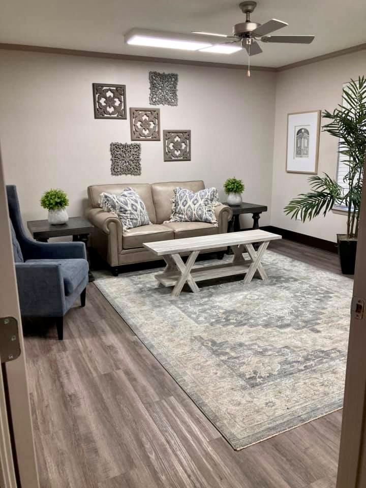 A cozy living room featuring a sofa, armchair, and coffee table with decorative artwork and plants.