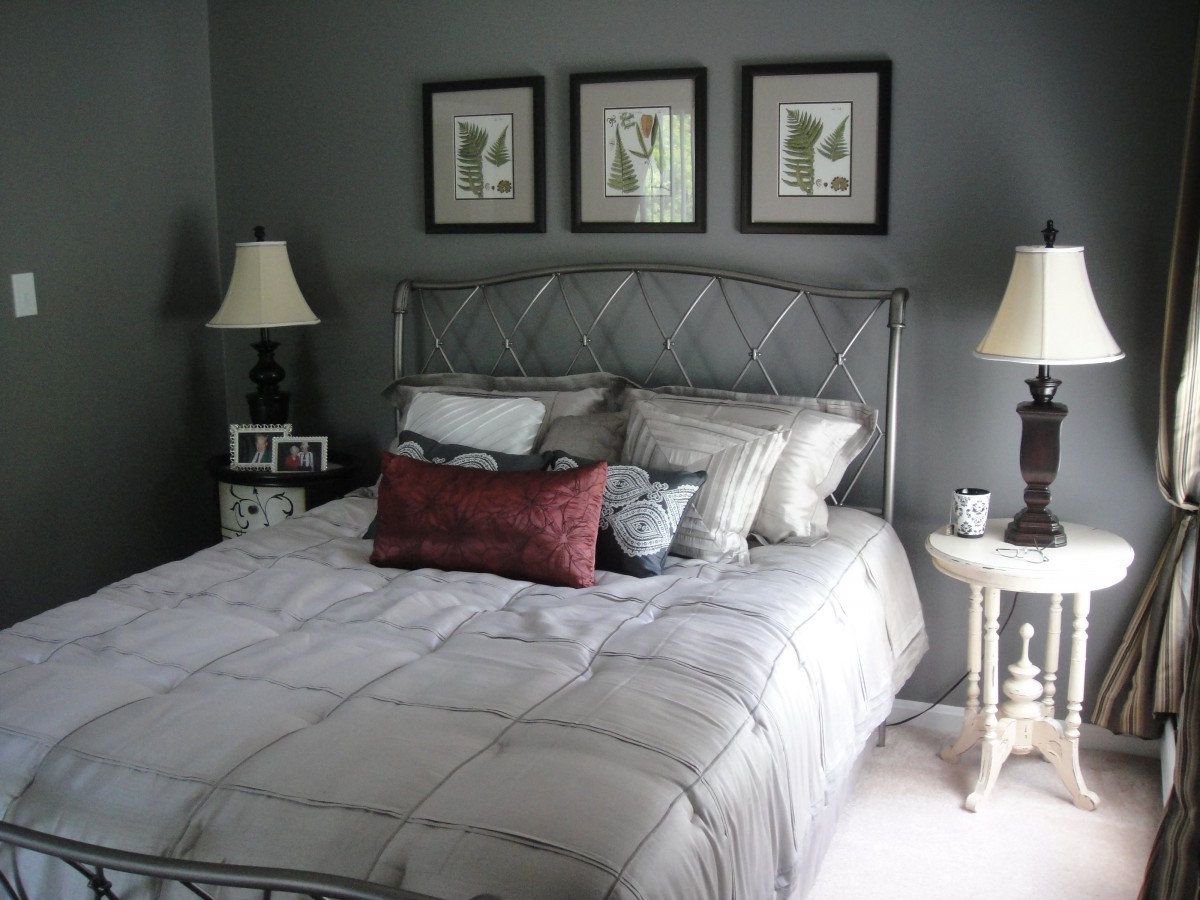 A cozy bedroom with a neatly made bed, decorated with pillows and flanked by two lamps on nightstands. Three framed artworks adorn the wall above the headboard.