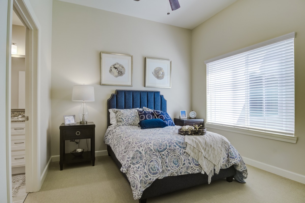 A modern bedroom with a blue upholstered headboard, decorative pillows, and framed artwork on the walls.