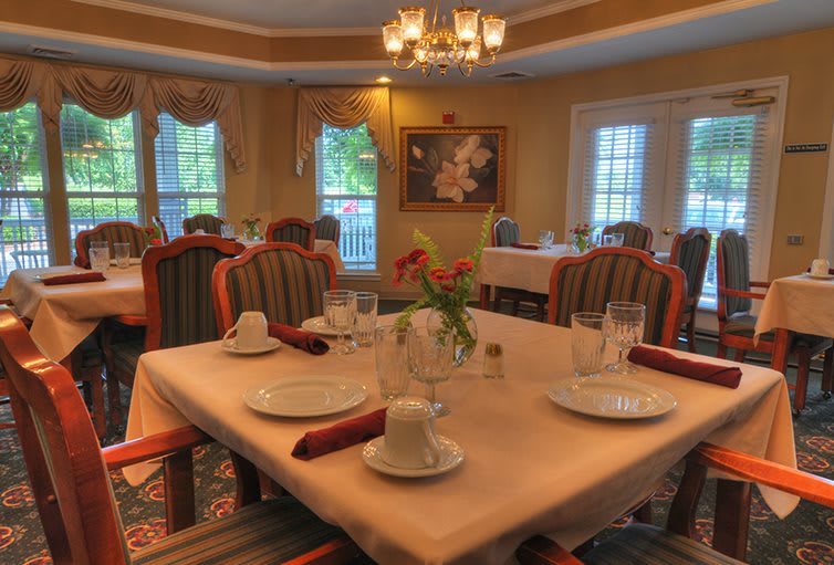 An elegant dining room with a neatly set table, featuring soft lighting and a chandelier.
