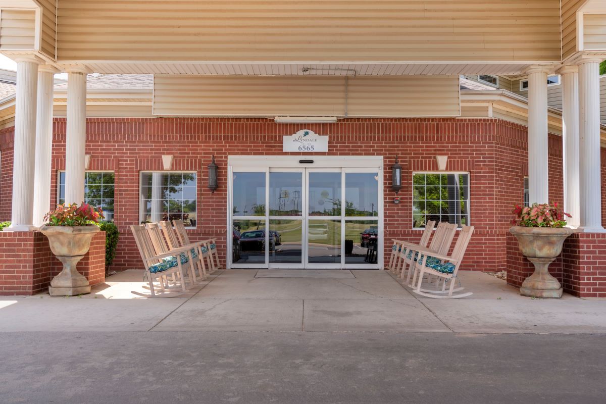 Entrance of a building with rocking chairs lined up along the brick wall.