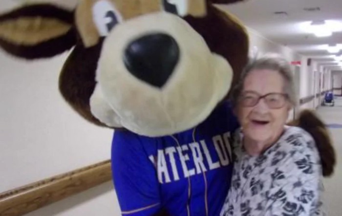 A person in a Waterloo mascot costume stands next to a smiling elderly woman indoors.