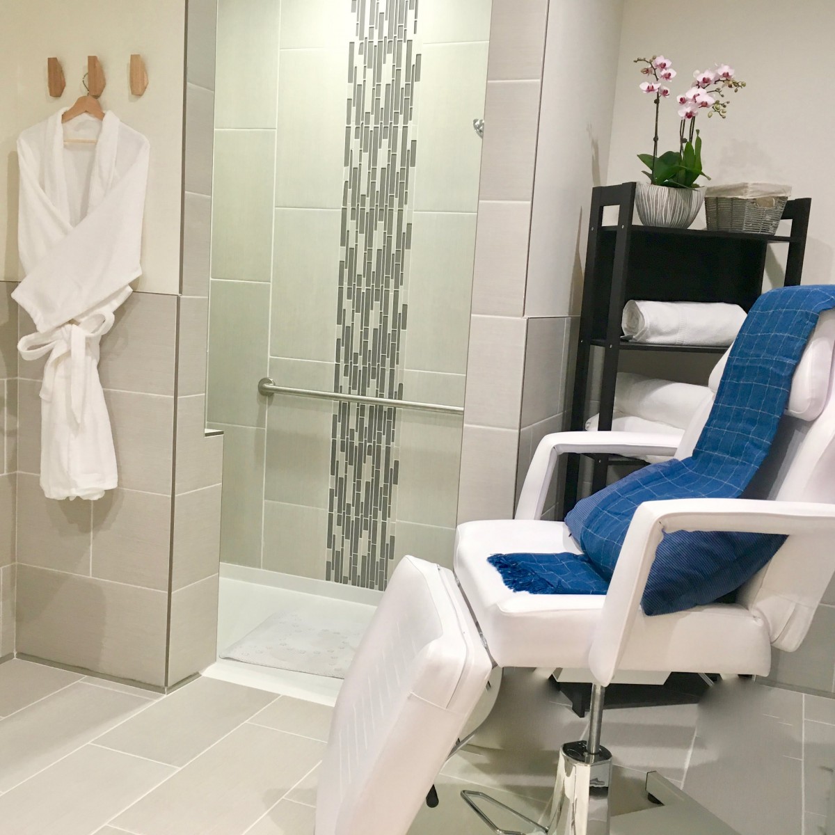 A serene spa room featuring a comfortable chair, bathrobe, towels, and an elegant shower.