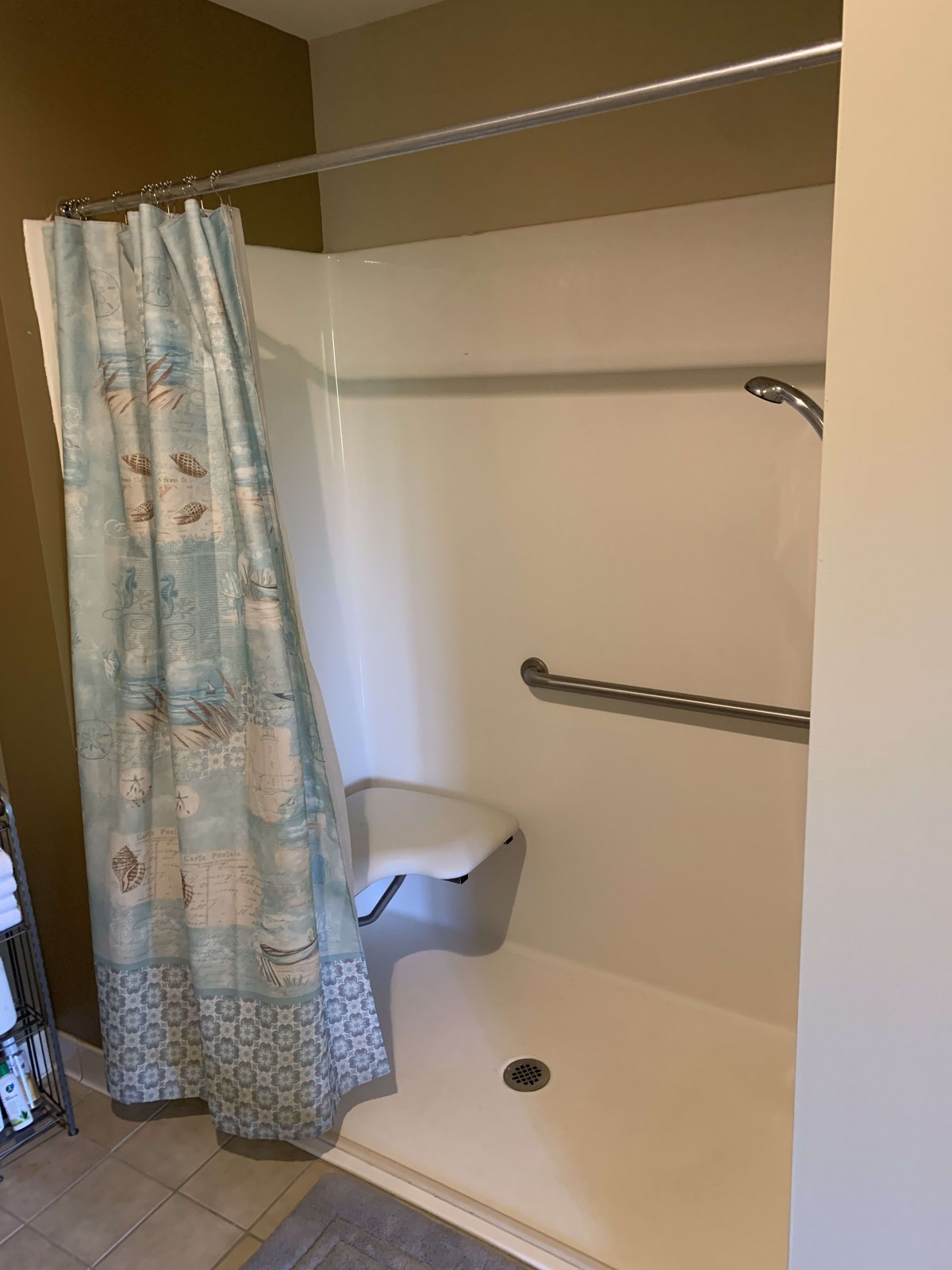 An accessible shower with a curtain, grab bar, and seating.
