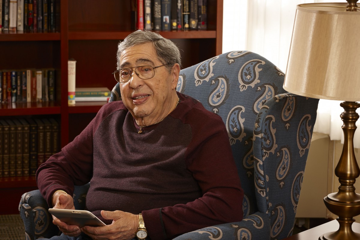 An older man sitting in an armchair with a book in his hand.