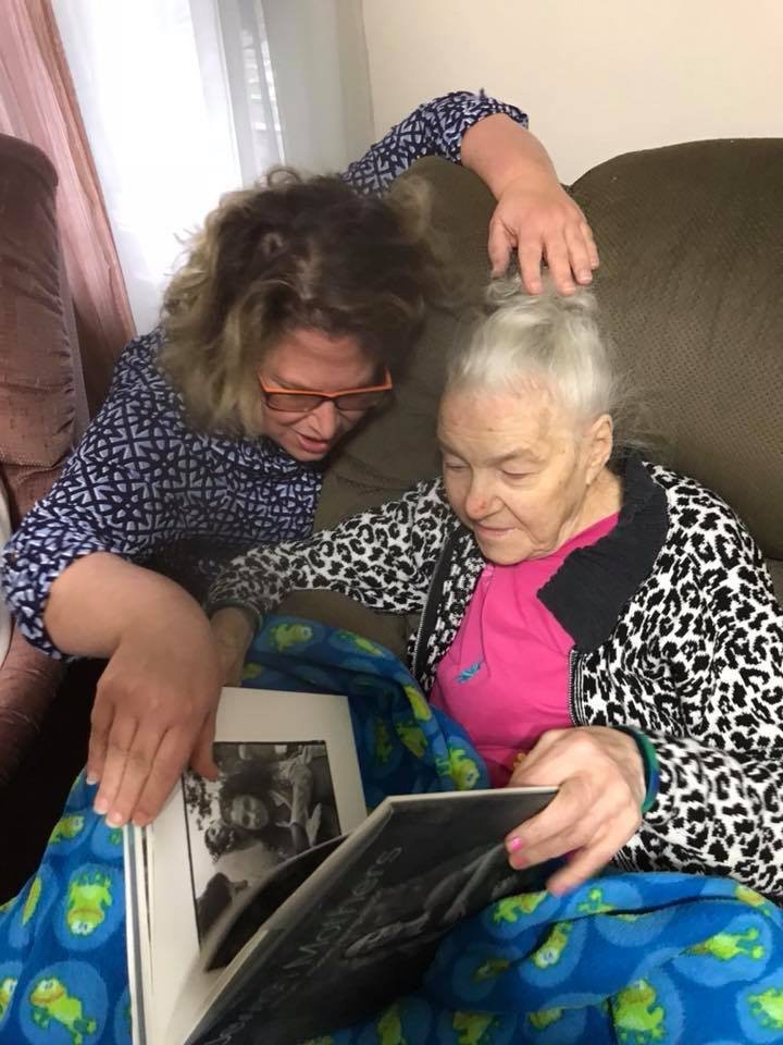 An elderly woman and her caregiver looking through a photo album together, sharing memories.