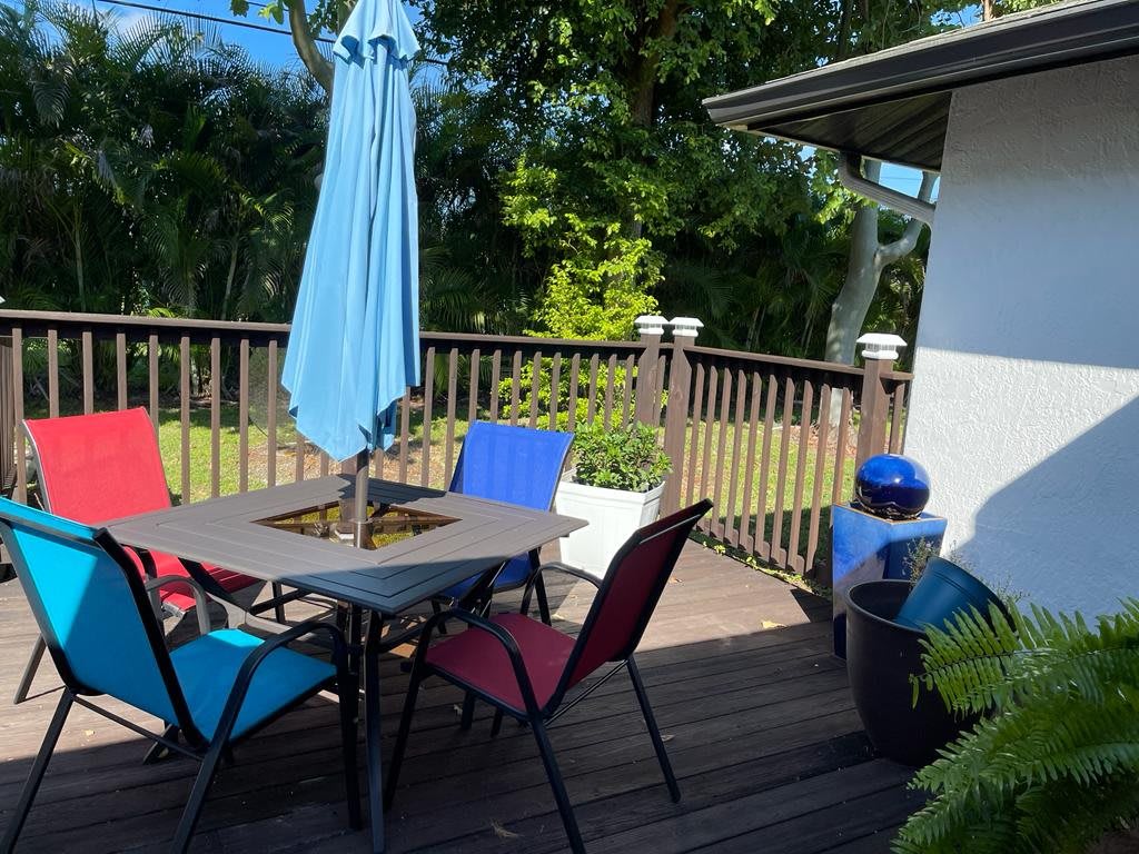 A sunny patio deck with colorful chairs and a blue umbrella, perfect for relaxing outdoors.
