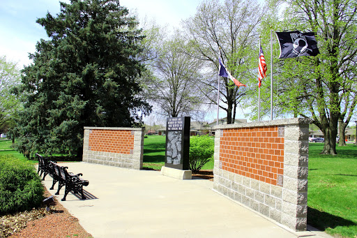 A serene memorial park featuring flags and brick walls, surrounded by lush greenery.