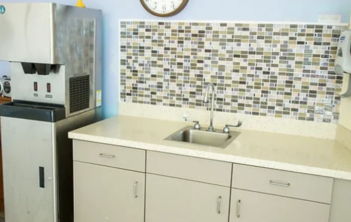 A small kitchen area with a tiled backsplash and a stainless steel sink on a white countertop.