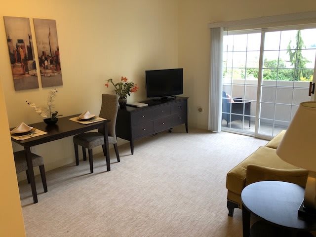 A cozy living room with a dining table, television, and sliding doors leading to a balcony.