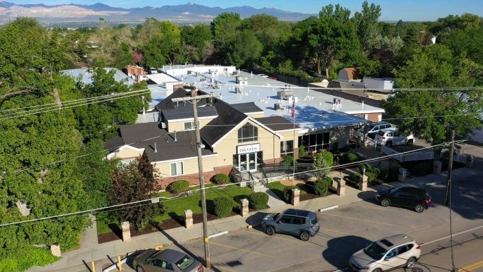 An aerial view of a suburban building surrounded by trees and parked cars.