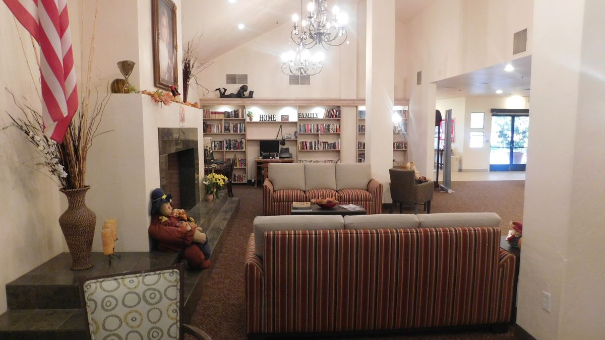 A cozy living room with a library, featuring bookshelves, sofas, a fireplace, and a chandelier.
