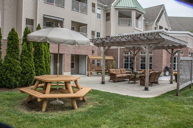A cozy outdoor patio area with picnic tables and seating under a pergola, set in an apartment complex.