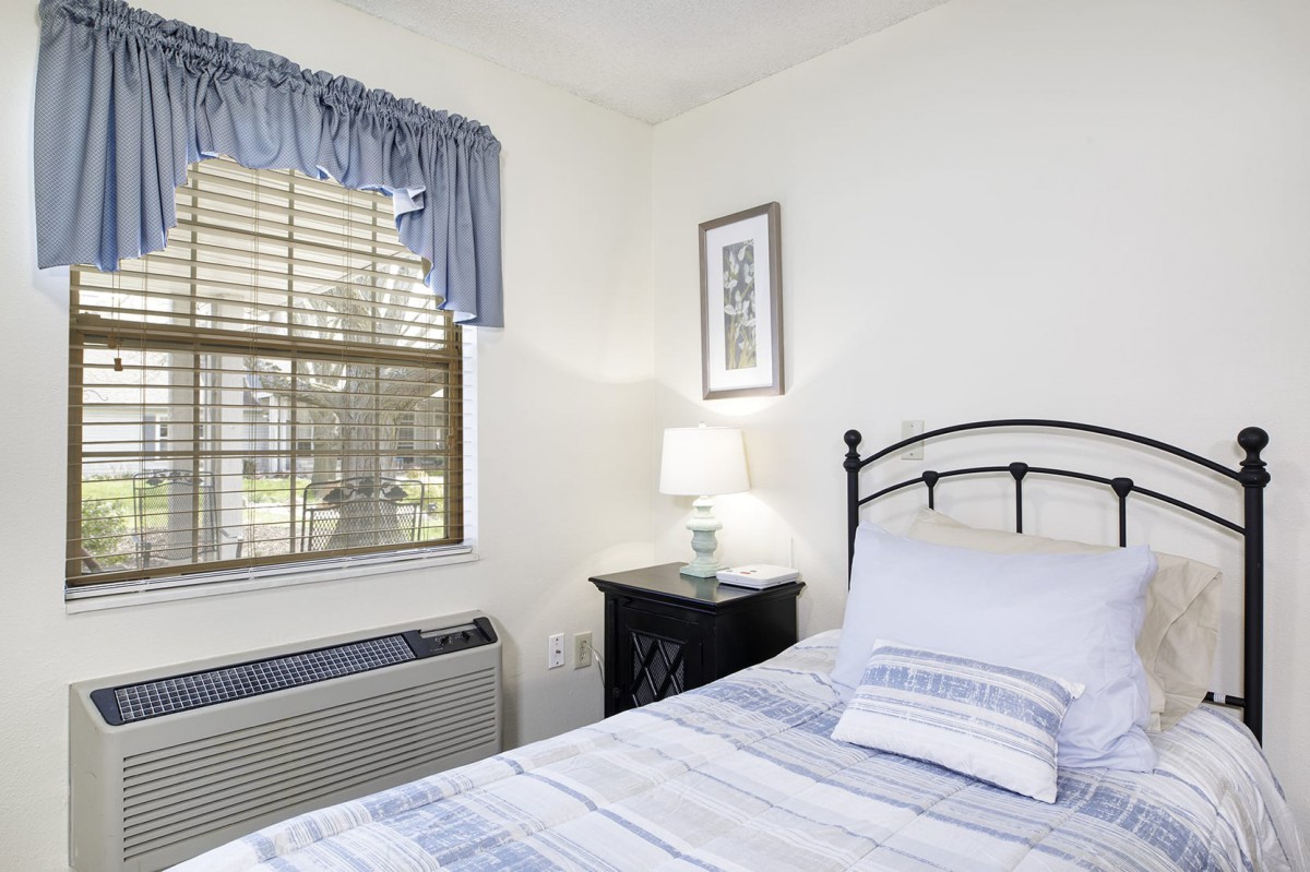 A cozy bedroom with a neatly made bed and a nightstand lamp by the window.