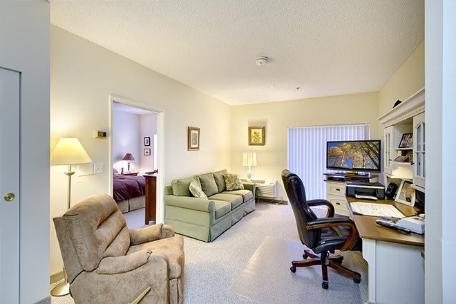 A cozy living room setup with an adjoining office space, featuring a sofa, armchair, desk, and computer.