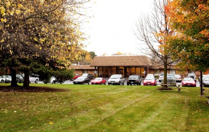A view of a building with a parking lot surrounded by trees in autumn.
