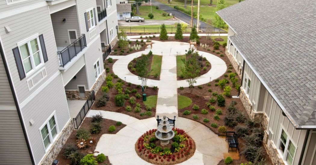 A beautifully designed courtyard with a symmetrical pathway, surrounded by lush greenery and a central fountain.