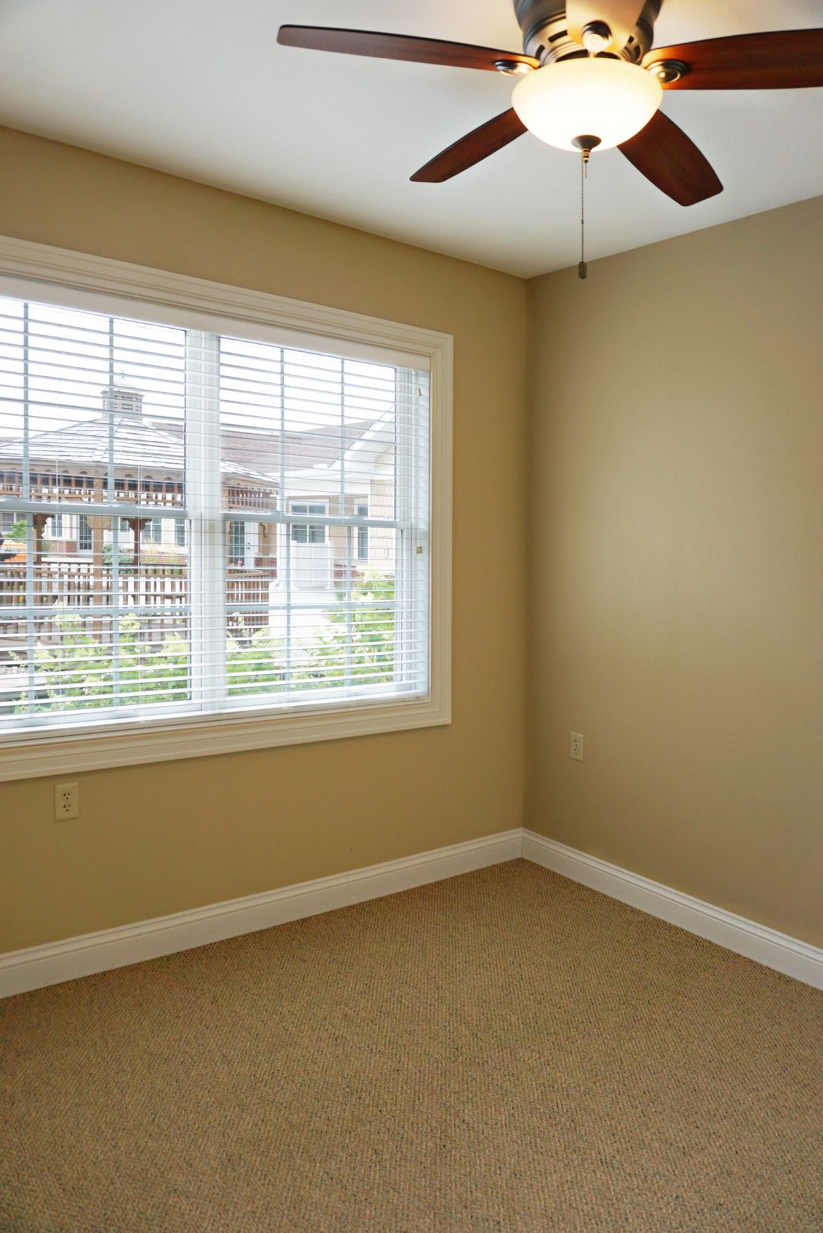 A bright empty room with beige walls and a large window letting in natural light.