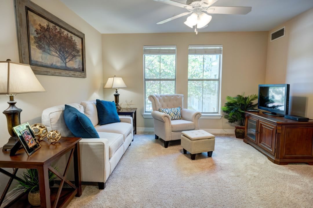A cozy living room with a sofa, armchair, and natural light from large windows.