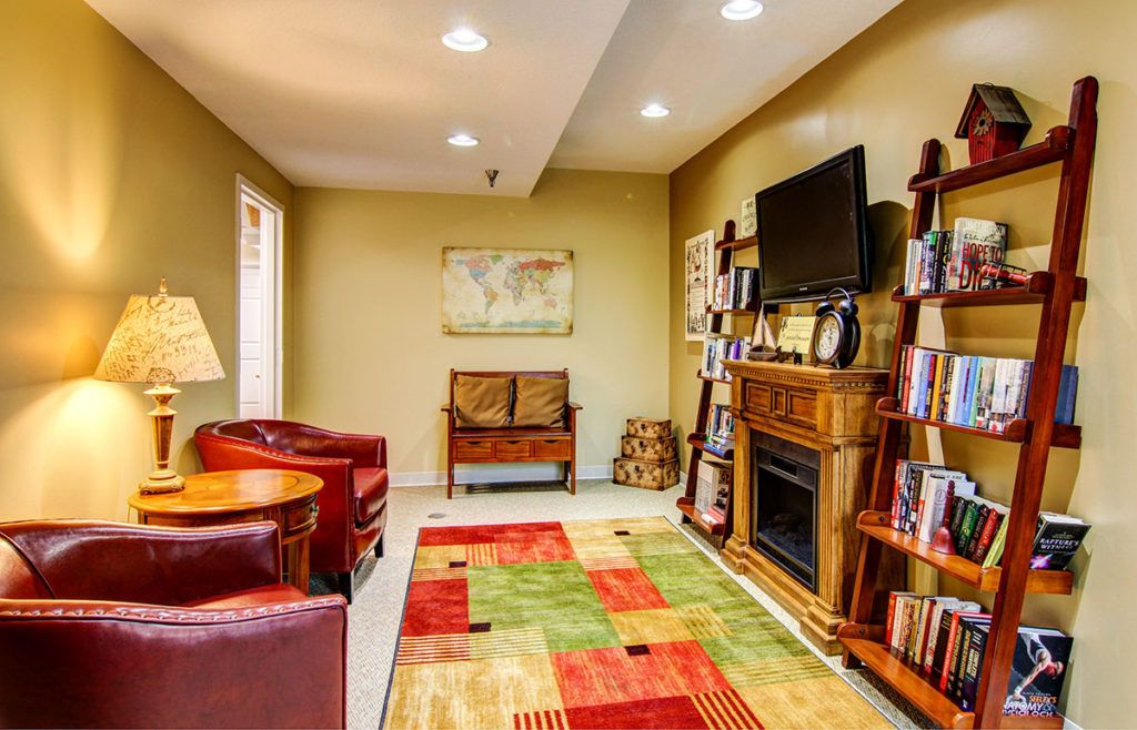 A cozy living room featuring comfortable seating, a colorful rug, and a fireplace with a television above.