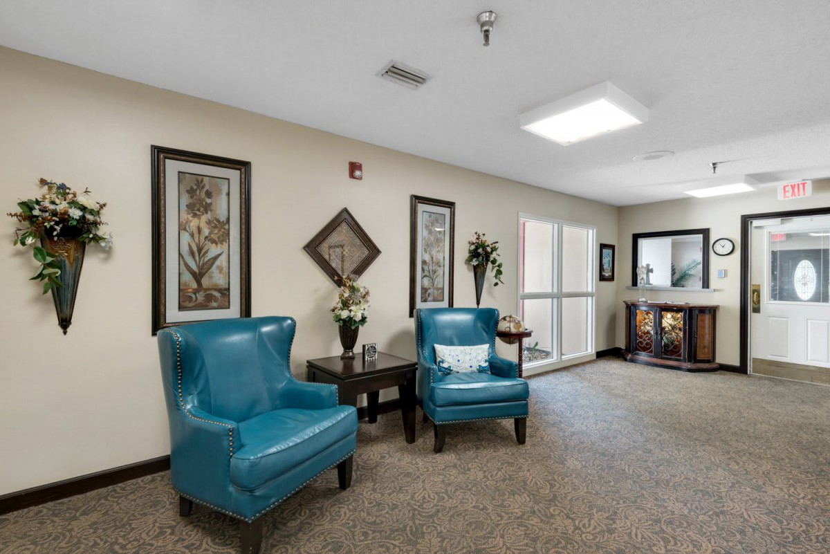 A cozy lounge area with teal chairs, floral decor, and framed artwork on the walls.