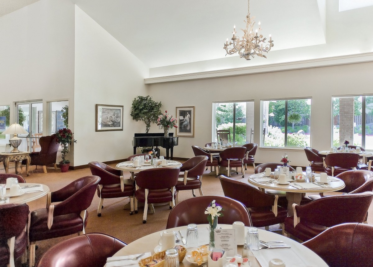 A spacious dining room with elegantly set tables and a chandelier, overlooking a scenic view through large windows.