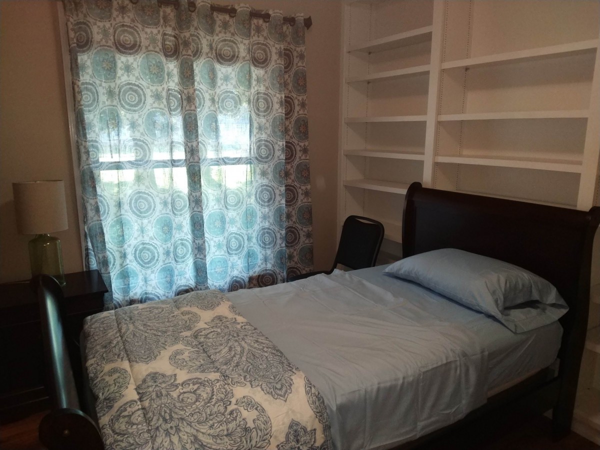 A cozy bedroom with a single bed, patterned curtains, and built-in shelves.