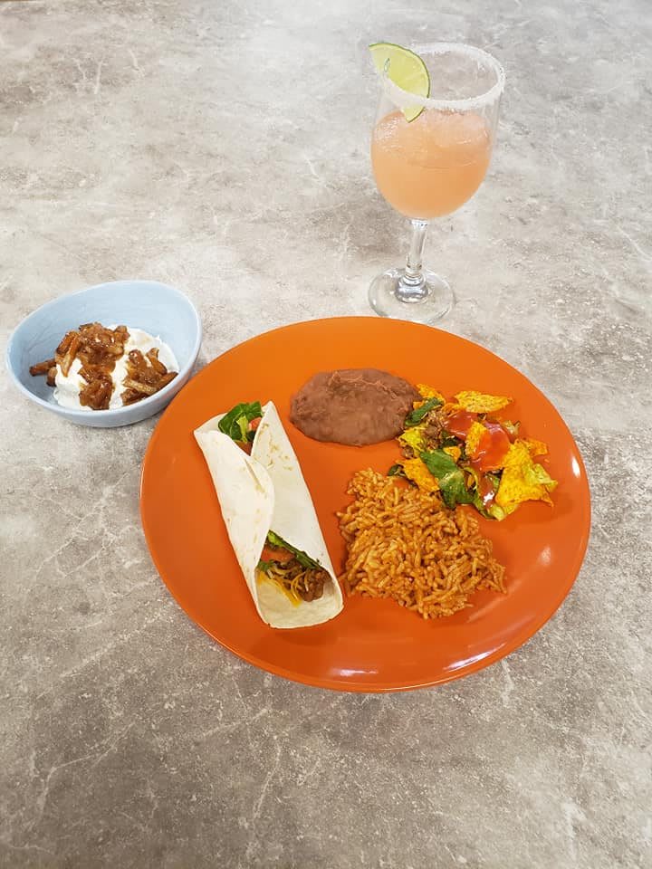 A colorful Mexican meal featuring a taco, rice, vegetables, refried beans on an orange plate, accompanied by a dessert and a refreshing beverage.